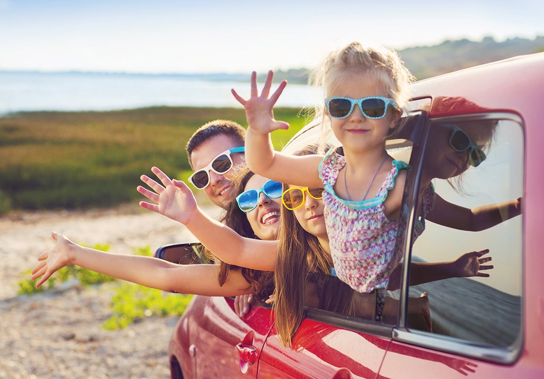 Family of 4 wearing sunglasses in red car on vacation