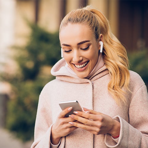 Woman smiling at cellphone while wearing wireless headphones